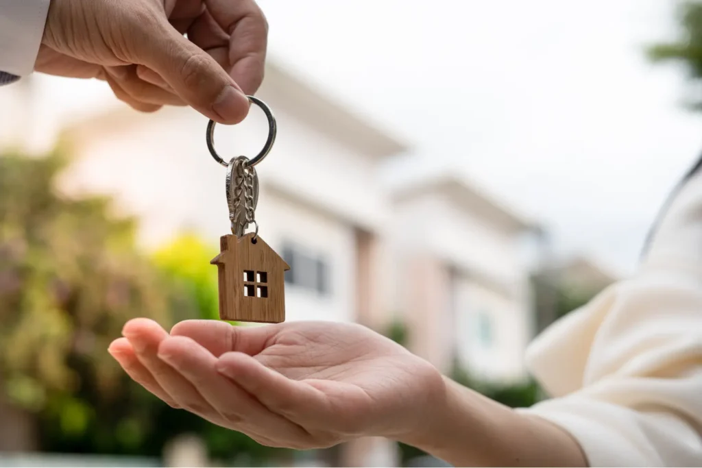 Landlord accounting software depicted by a person handing over house keys with a home in the background.