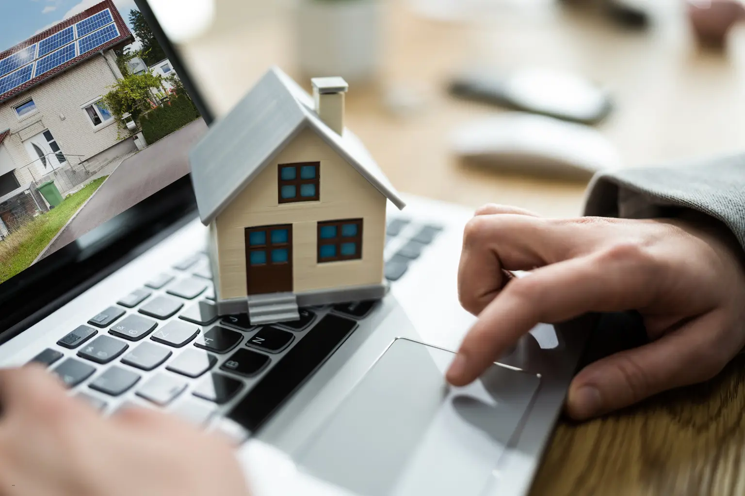 property management software concept with a miniature house on a laptop keyboard beside a user’s hand