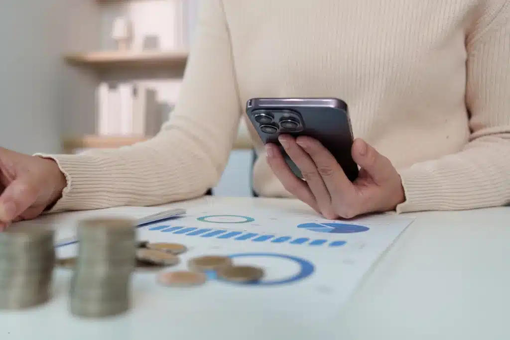 Landlord income and expense tracker showing smartphone use over financial charts, coins, and budget reports on desk.