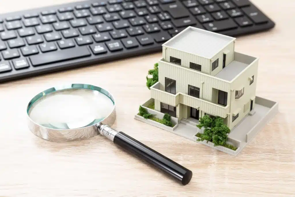 Manage rental properties online with property search and inspection concept—house model, magnifying glass, and keyboard on desk.