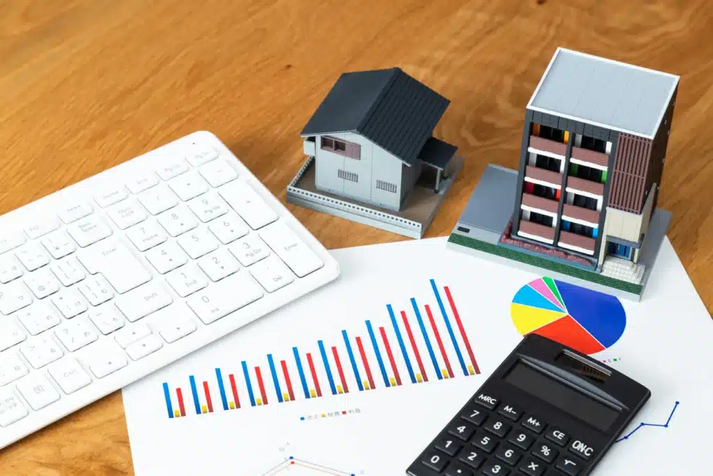 Property management system concept with rental house models, calculator, and financial charts on desk for tracking income and expenses.