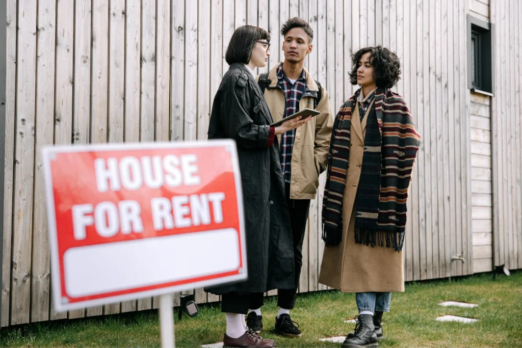 Landlord property management depicted by a leasing agent discussing rental details with prospective tenants beside a house for rent sign.