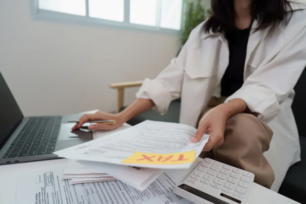 Property management system being accessed by a woman reviewing tax documents and financial paperwork on a laptop at her desk