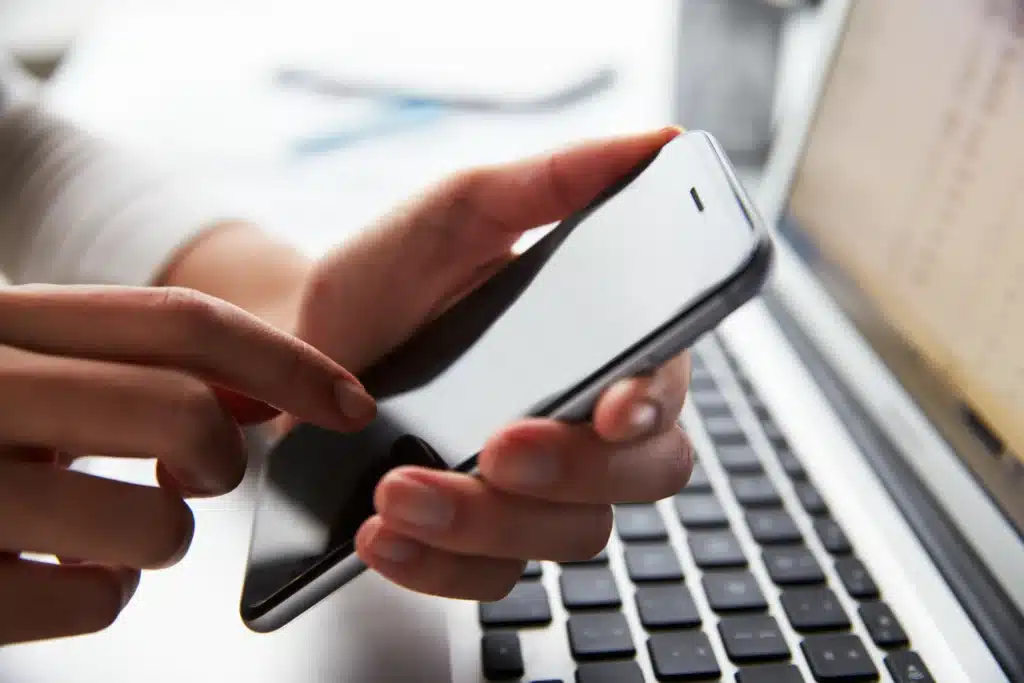 Rent payment app for landlords illustrated by a close-up of a person using a smartphone beside a laptop.