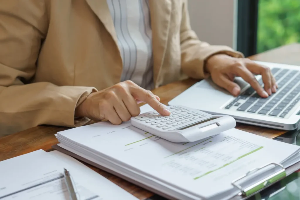 Rental property mileage and expense tracking by a professional using a calculator and laptop alongside financial documents at a desk