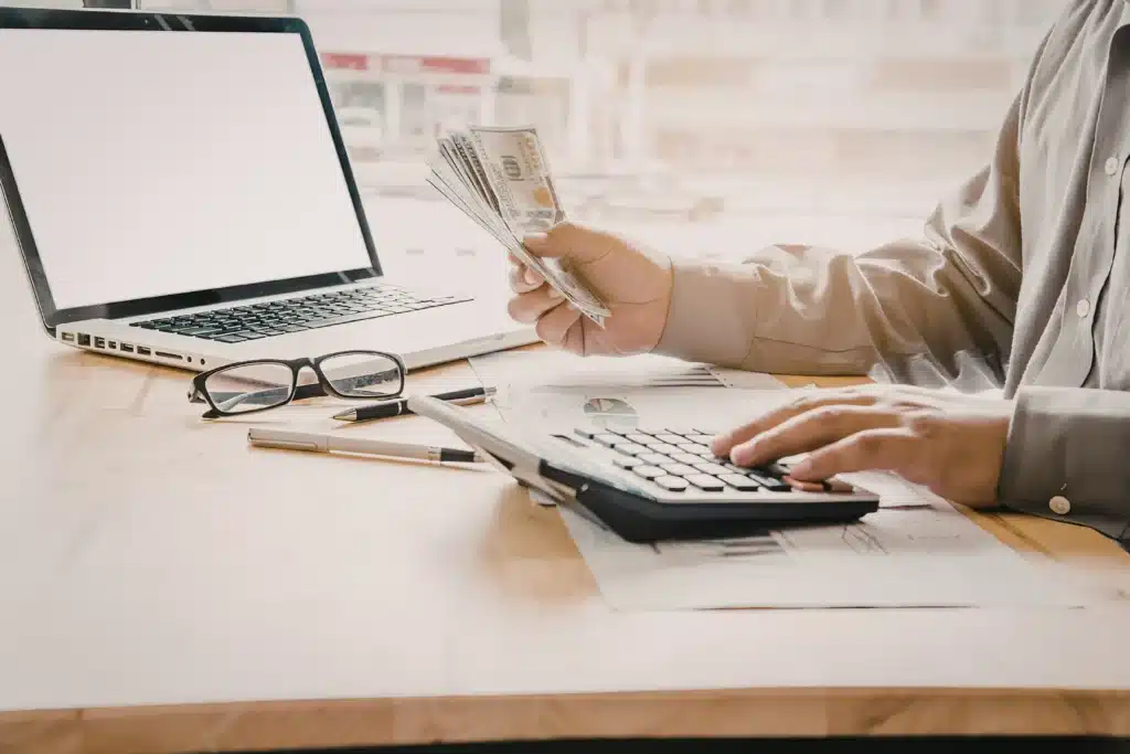landlord counting cash while working on a building maintenance checklist with laptop and calculator