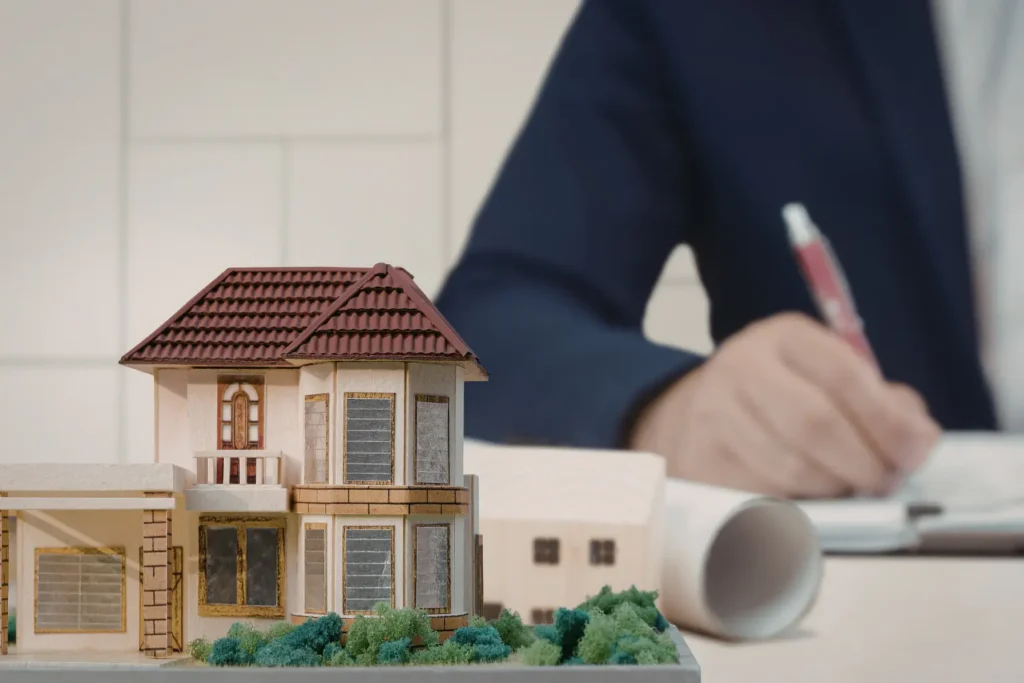 Landlord mileage tracking and property documentation managed by a professional writing notes beside a detailed architectural house model on a desk