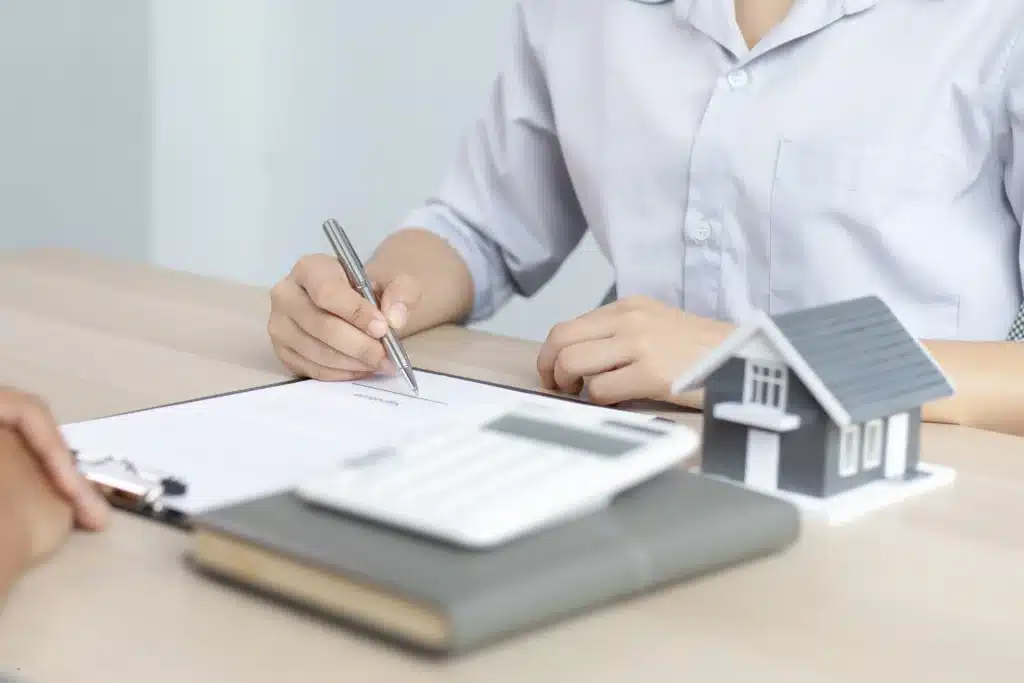 person signing a contract to manage multiple properties with a house model on the desk