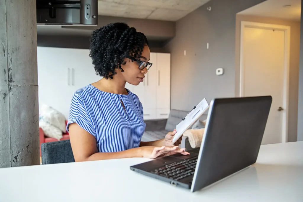 Mileage tracking for rental properties managed by a woman reviewing a clipboard while working on a laptop at home
