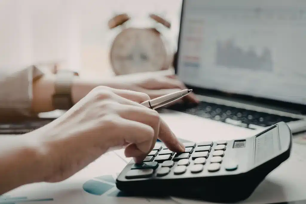 person using a calculator and laptop to manage a property management system