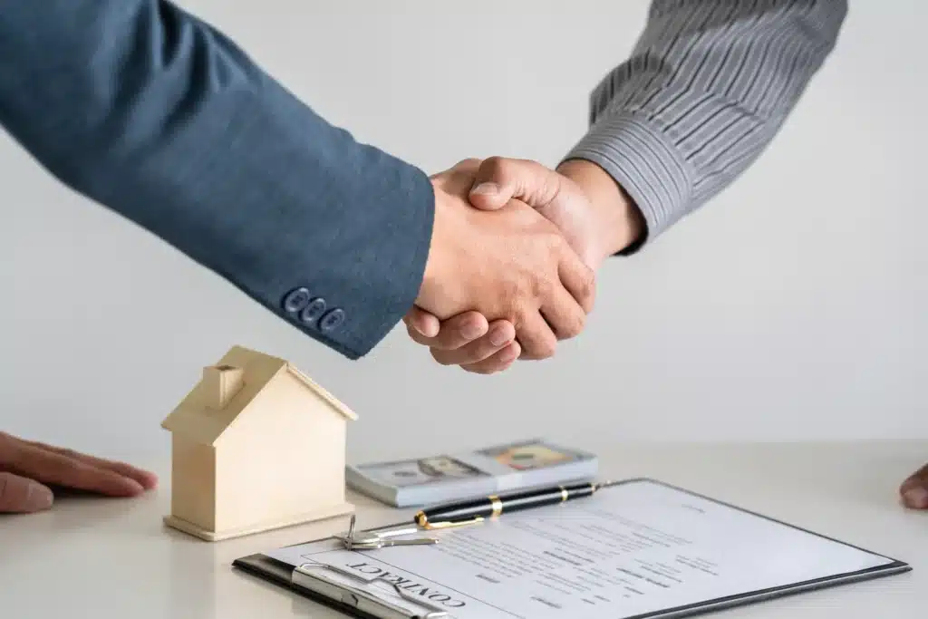 landlord and tenant shaking hands over rent collection agreement with house model and contract on desk