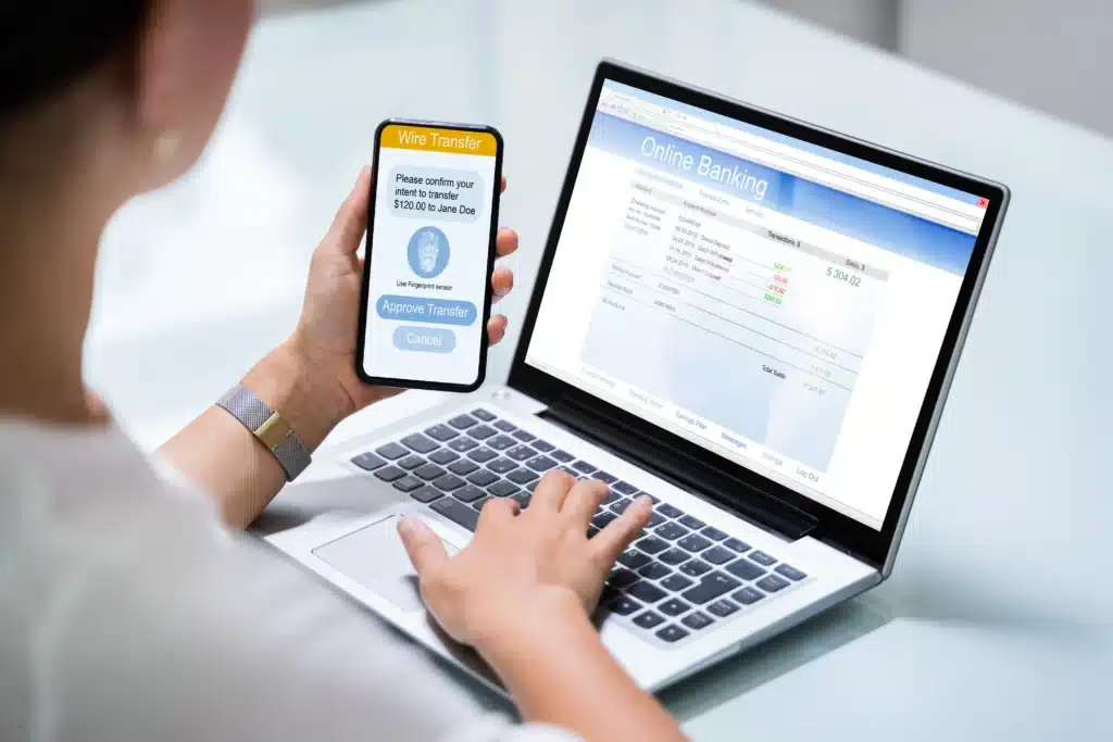 woman using a rent collection app to approve a wire transfer via online banking on laptop and smartphone