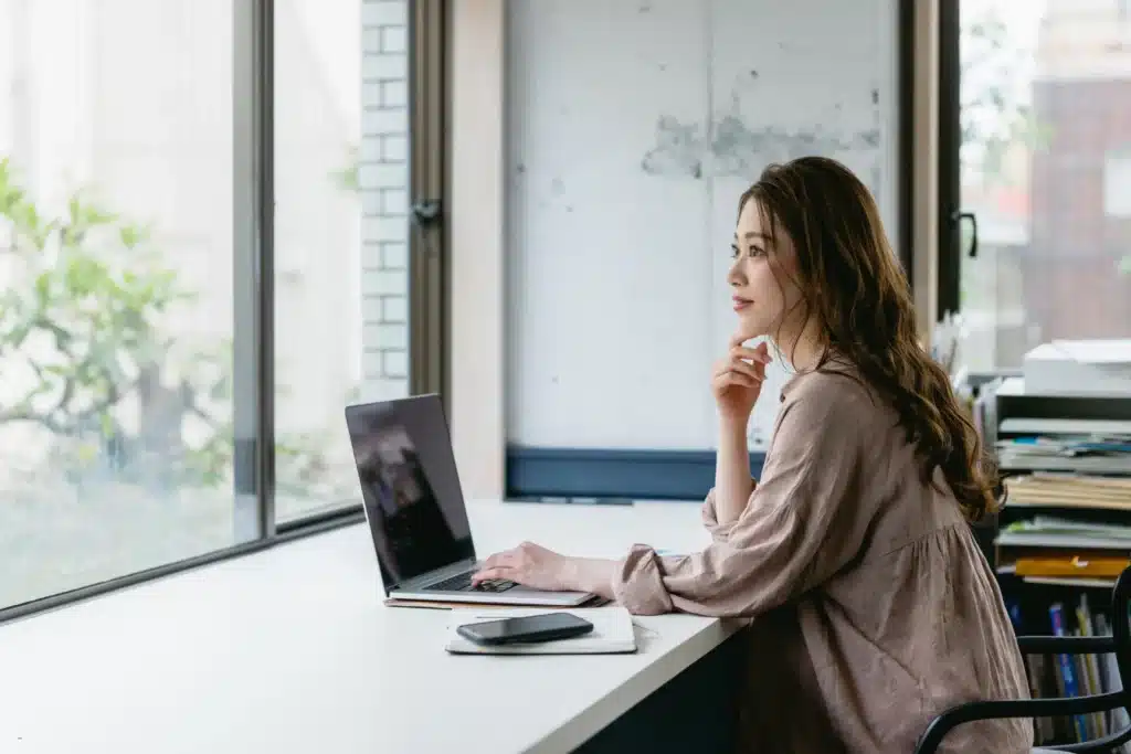 woman thoughtfully reviewing rental property management options on laptop by office window